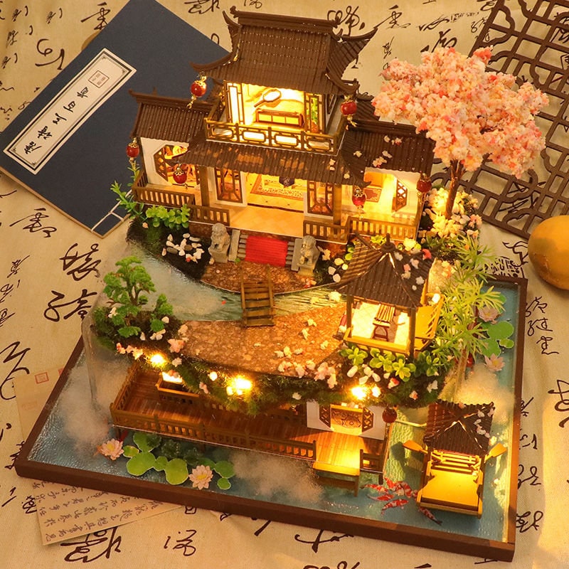 May include: A miniature wooden dollhouse with a traditional Chinese design, featuring a multi-level structure, a red roof, and a small garden with a pond and a bridge. The dollhouse is lit with small LED lights and has a cherry blossom tree.