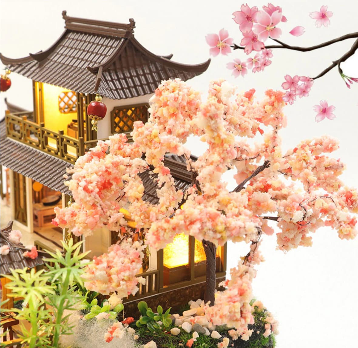 May include: A miniature wooden dollhouse with a traditional Chinese design, featuring a brown roof, white walls, and a small garden with a pink cherry blossom tree. The dollhouse has a lit interior and is decorated with small details like lanterns and windows.
