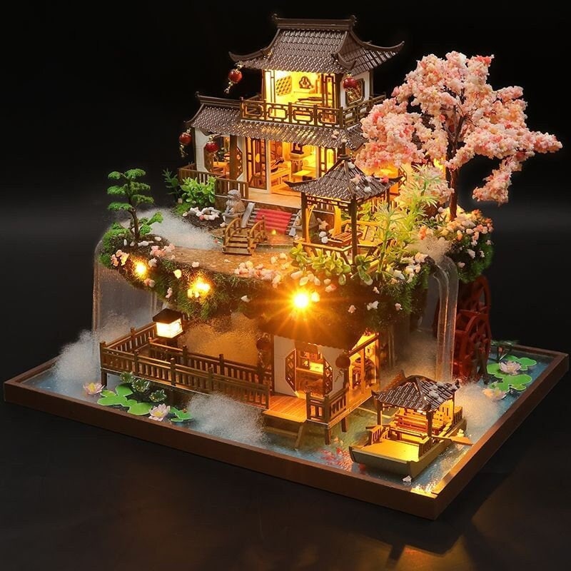May include: A miniature wooden dollhouse with a traditional Chinese design, featuring a multi-level structure with a pagoda roof, a waterfall, a bridge, and a cherry blossom tree. The dollhouse is illuminated with warm white LED lights, creating a cozy and enchanting atmosphere.