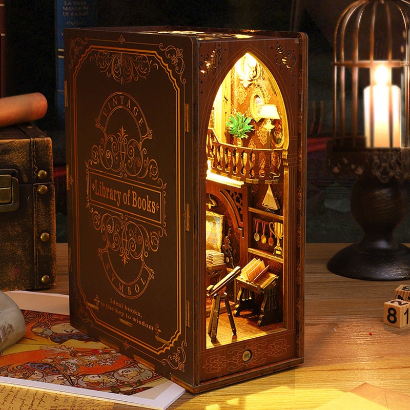 May include: A wooden book-shaped box with a miniature library scene inside. The box is decorated with gold accents and the words "Vintage Library of Books".