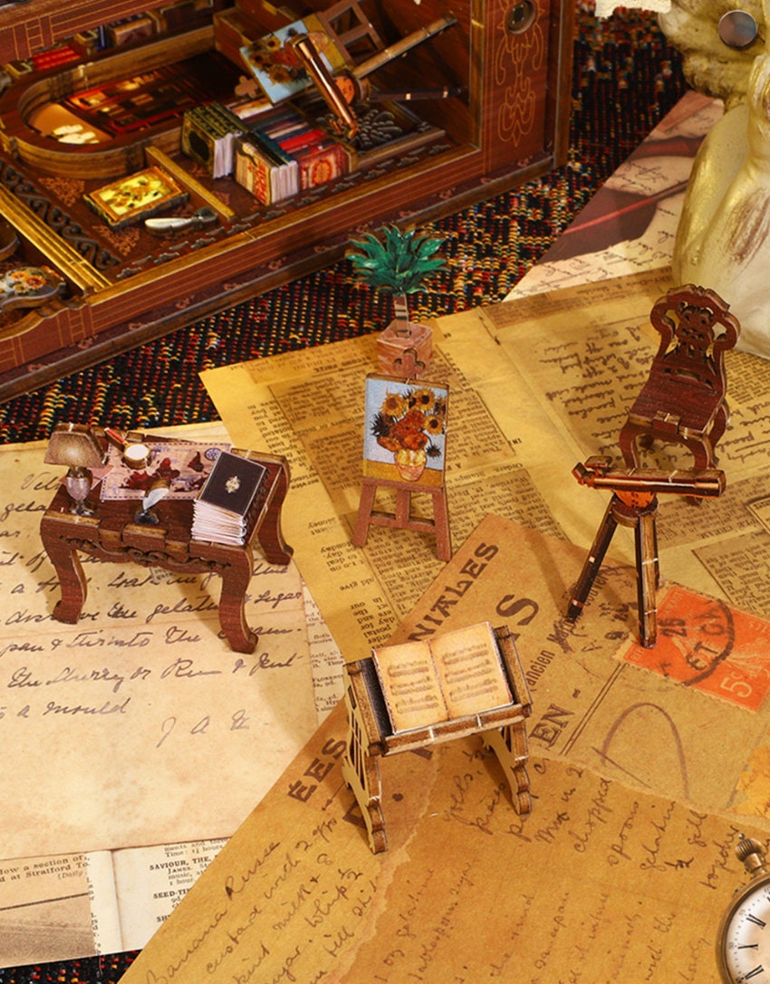 May include: A miniature wooden easel with a painting of sunflowers, a miniature wooden music stand with a book, and a miniature wooden chair with a violin on a table. All of the items are on a brown surface with old paper and a watch.
