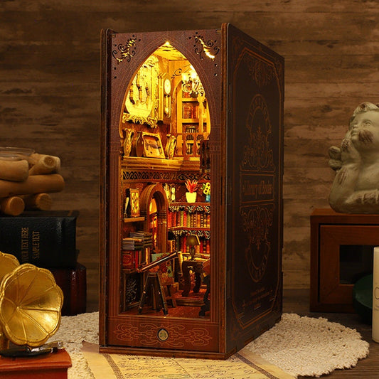 May include: A wooden book-shaped box with a miniature library inside. The box is brown with gold accents and the text "A Library of Books" on the side. The miniature library is lit up and features bookshelves, a desk, and a chair.