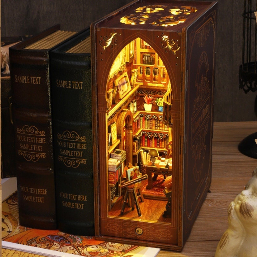 May include: A wooden book-shaped box with a miniature library scene inside. The box is lit from within, illuminating the shelves of books, a desk, and a chair. The box is made to look like a vintage book with a brown leather cover and gold lettering.