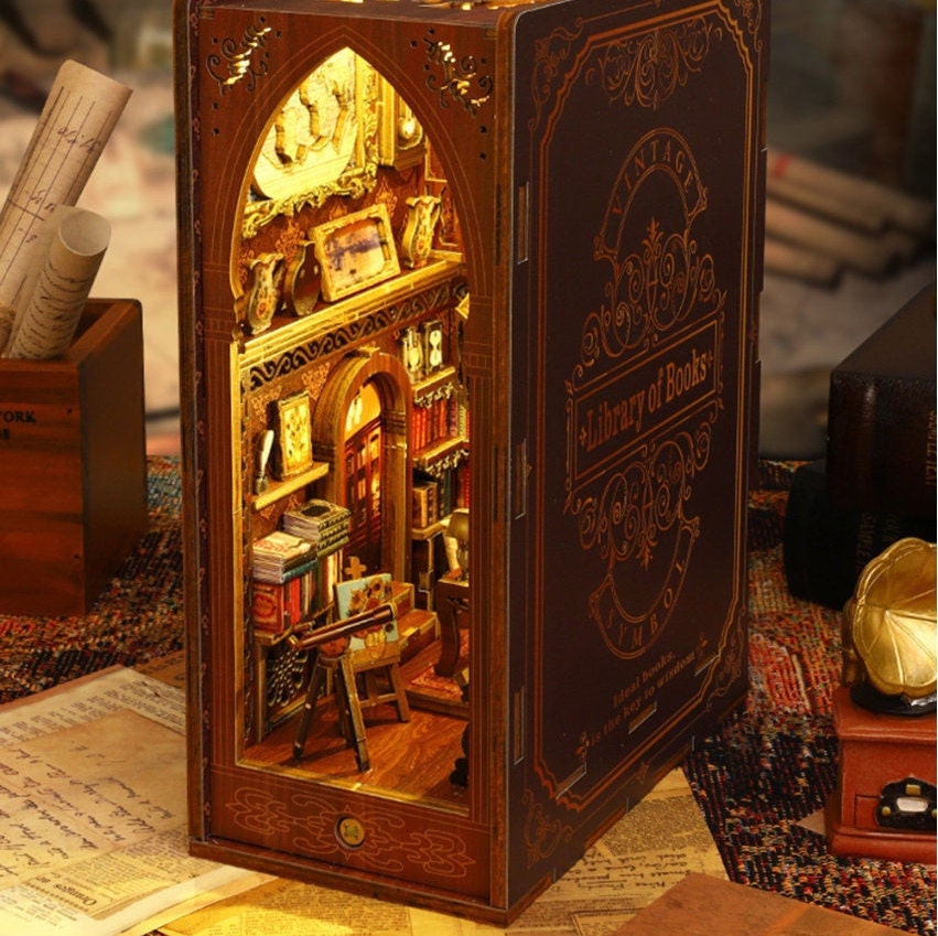 May include: A miniature wooden book-shaped box with a detailed interior scene of a library. The box is open, revealing a small, intricately crafted library with bookshelves, a ladder, and a table. The front of the box features the text "Vintage Library of Books".
