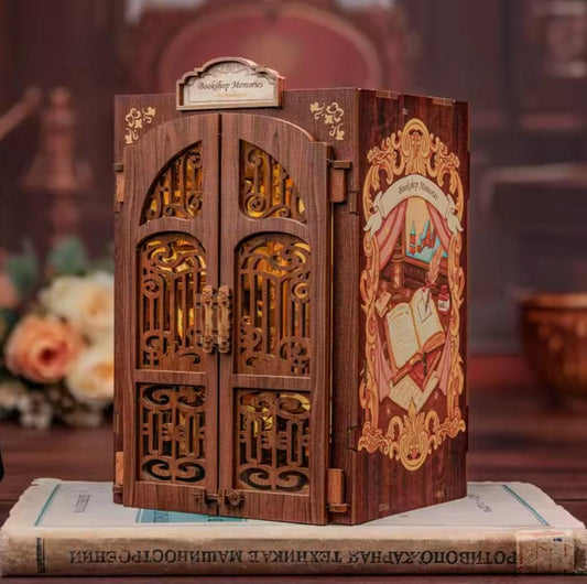 May include: A wooden book-shaped box with a decorative front panel featuring a bookshelf with open doors and a book with a quill pen and inkwell. The box is labeled "Bookshop Memories".