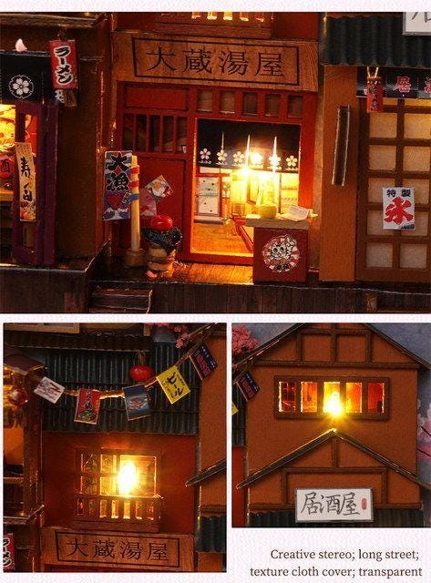 May include: A miniature Japanese street scene with illuminated buildings, signs, and lanterns. The scene includes a ramen shop and a bar, with detailed architectural elements and Japanese text. The overall color scheme is warm, with a focus on the illuminated interiors.