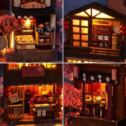 May include: Miniature Japanese shop models with intricate details. The models feature traditional architecture, illuminated interiors, and cherry blossom accents. The shops include a bakery, a ramen shop, and a sushi restaurant.