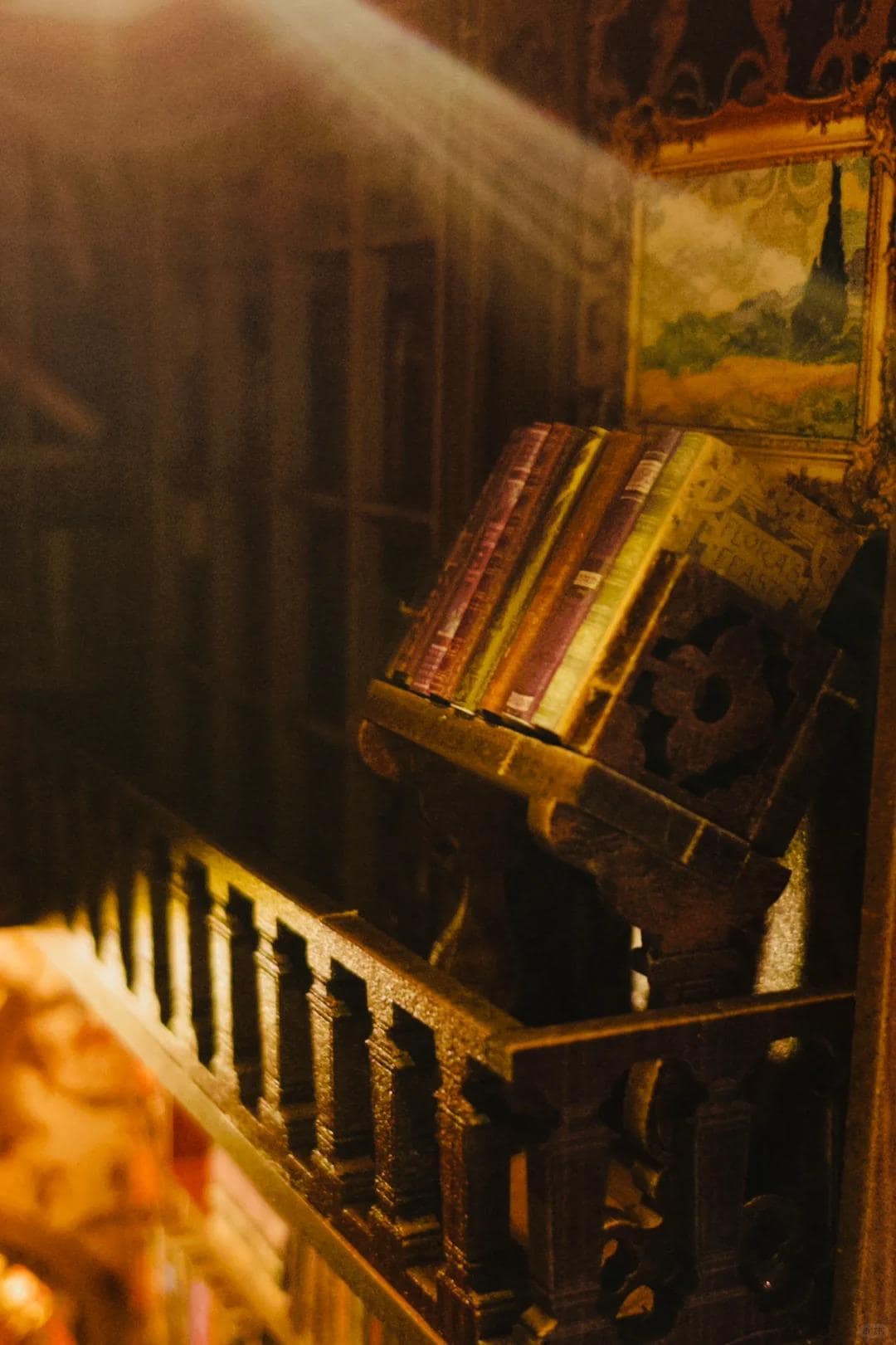 May include: A wooden book stand with a decorative design holds a stack of vintage books. The stand is in a dimly lit room with a painting on the wall behind it.
