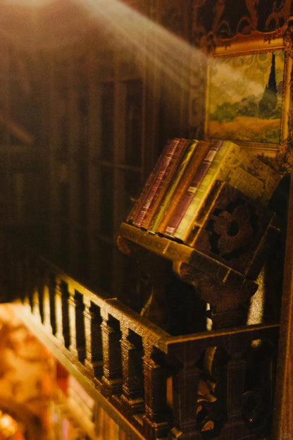 May include: A wooden book stand with a decorative design holds a stack of vintage books. The stand is in a dimly lit room with a painting on the wall behind it.