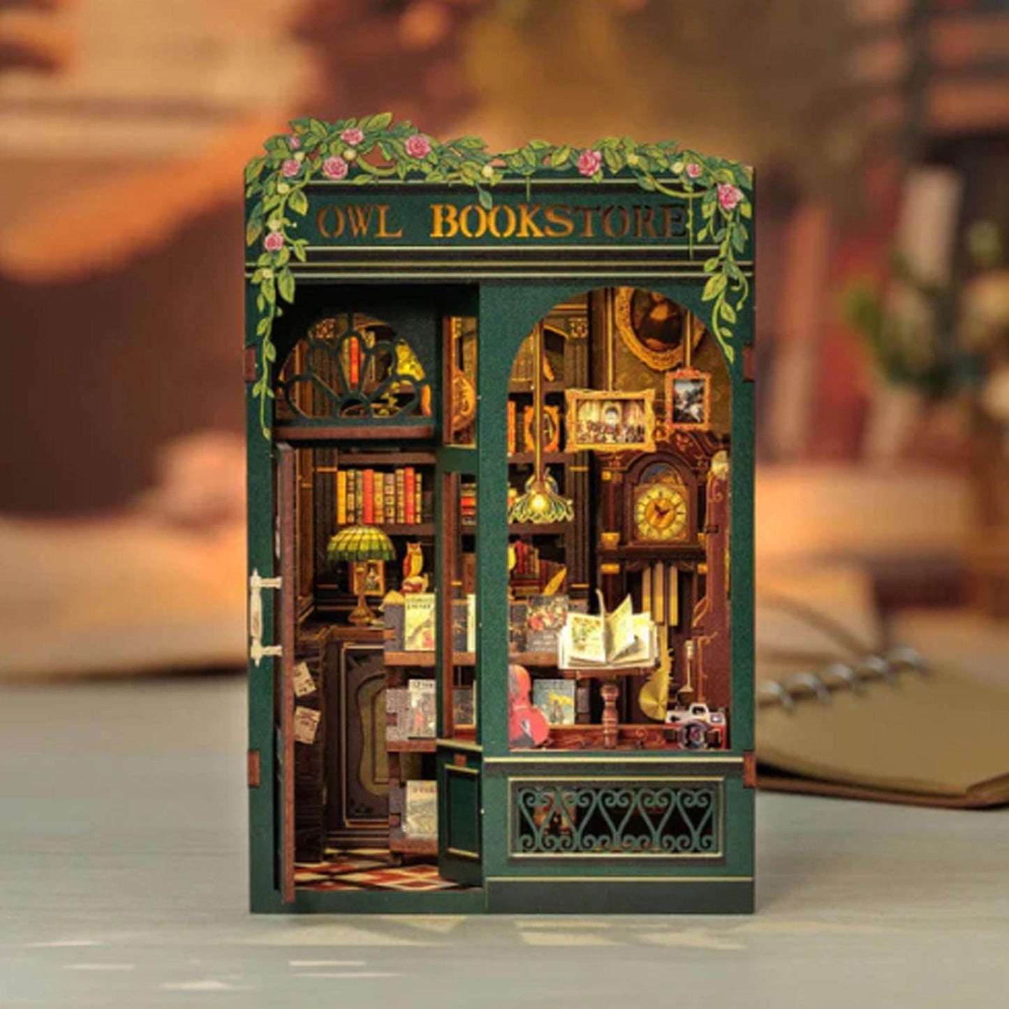 May include: A miniature wooden model of an owl bookstore with a green exterior and a sign that reads "Owl Bookstore". The model features a detailed interior with bookshelves, a counter, and a clock.