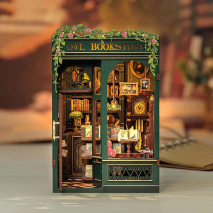 May include: A miniature wooden model of an owl bookstore with a green exterior and a sign that reads "Owl Bookstore". The model features a detailed interior with bookshelves, a counter, and a clock.