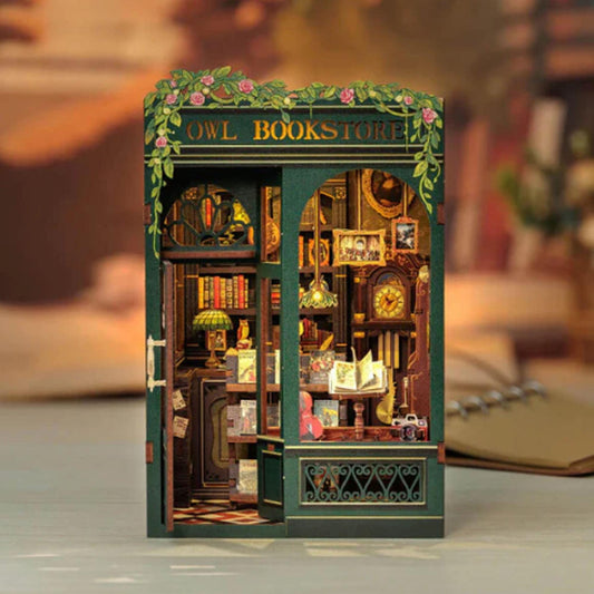 May include: A miniature wooden model of an owl bookstore with a green exterior and a sign that reads "Owl Bookstore". The model features a detailed interior with bookshelves, a counter, and a clock.
