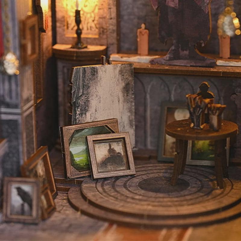 May include: Miniature diorama of an artist's studio with framed paintings, a small wooden table, and a weathered stone wall. The scene includes a candlelit ambiance, creating a warm, inviting atmosphere. The artwork features landscapes and a silhouette.
