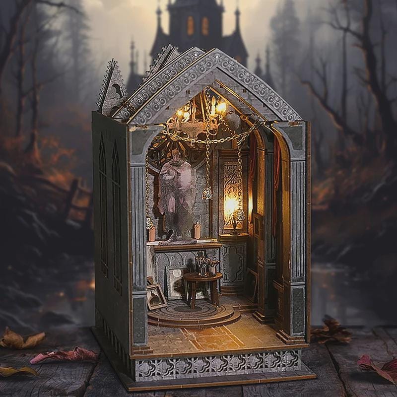 May include: A miniature gothic-style diorama with a detailed interior, featuring a statue, small table, and ornate architectural elements. The diorama is illuminated with warm lighting, creating a mysterious atmosphere. The exterior is gray with decorative trim, set against a blurred forest backdrop.
