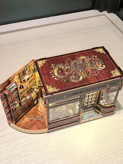 May include: A detailed, three-dimensional model of a Corner Coffee Shop. The model features a brown facade with decorative gold accents, a glass display window, and a detailed interior with miniature furniture and books. The roof has an ornate design.