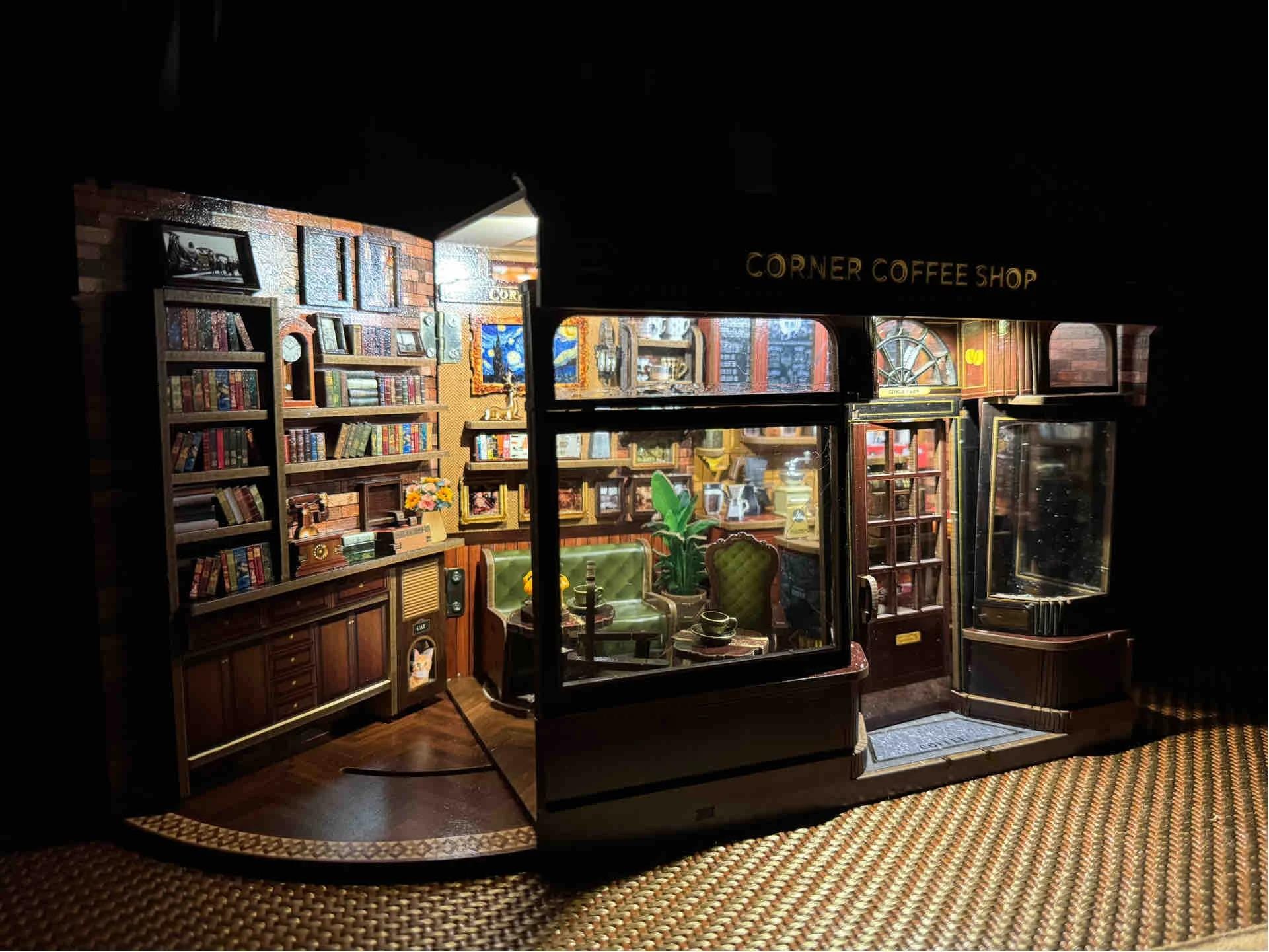 May include: Miniature corner coffee shop diorama with detailed interior. Features bookshelves, framed art, and seating. The shop's exterior has a sign that reads "CORNER COFFEE SHOP". The scene is warmly lit, creating a cozy atmosphere.