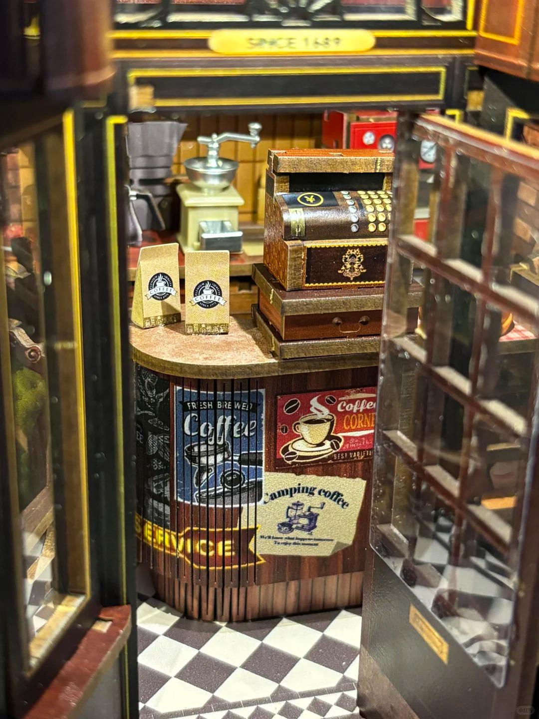 May include: Miniature coffee shop diorama with a vintage aesthetic. Features a coffee grinder, cash register, and coffee bags. The counter displays coffee-themed posters. The shop has a checkered floor and a sign that reads "SERVICE".