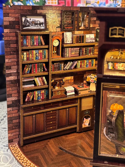 May include: A miniature wooden library scene with a brick wall backdrop. The scene includes bookshelves filled with tiny books, a grandfather clock, framed pictures, and a small cat house. The overall color scheme is warm, with browns and reds.