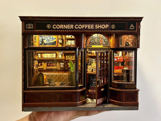 May include: Miniature Corner Coffee Shop model with detailed interior and exterior features. The shop has a dark wood facade, glass windows, and the text "CORNER COFFEE SHOP" above the entrance. Inside, there are miniature paintings, furniture, and a coffee machine.