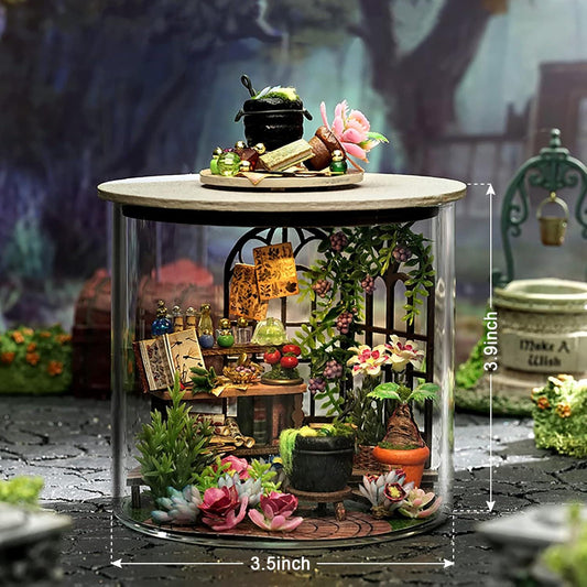 May include: A miniature diorama inside a glass cylinder, featuring a detailed witch's apothecary scene. The scene includes tiny books, bottles, plants, and a cauldron. The cylinder is 3.5 inches wide and 3.9 inches tall.