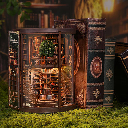 May include: A miniature, illuminated bookshelf diorama with a spiral staircase and a central tree. The diorama is encased in a dark wood frame, with a glass front. Several antique-looking books are placed next to the diorama, with ornate gold detailing.